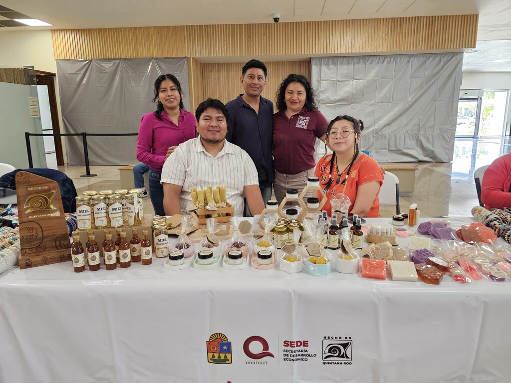Equipo de Miel de Flores Mayas detrás de una mesa con miel y productos artesanales